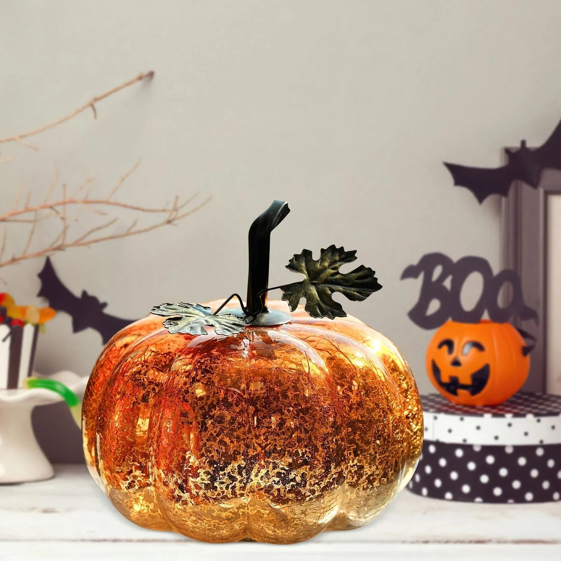 Decorative glass pumpkin with metal leaves on table, Halloween decor with jack-o'-lantern and bats