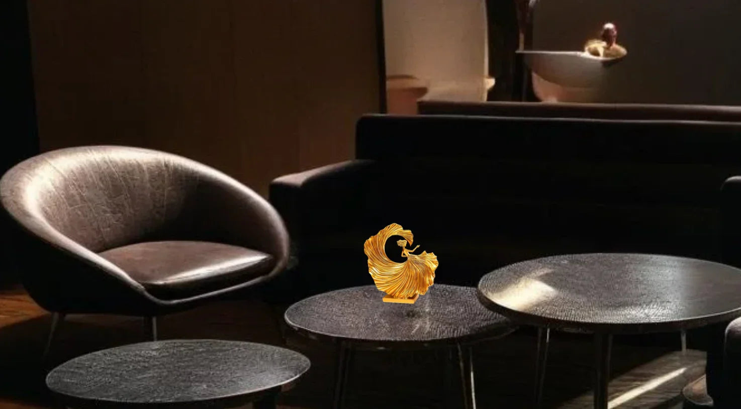 Modern living room with dark leather armchair, black sofa, round textured coffee tables, and golden decorative sculpture