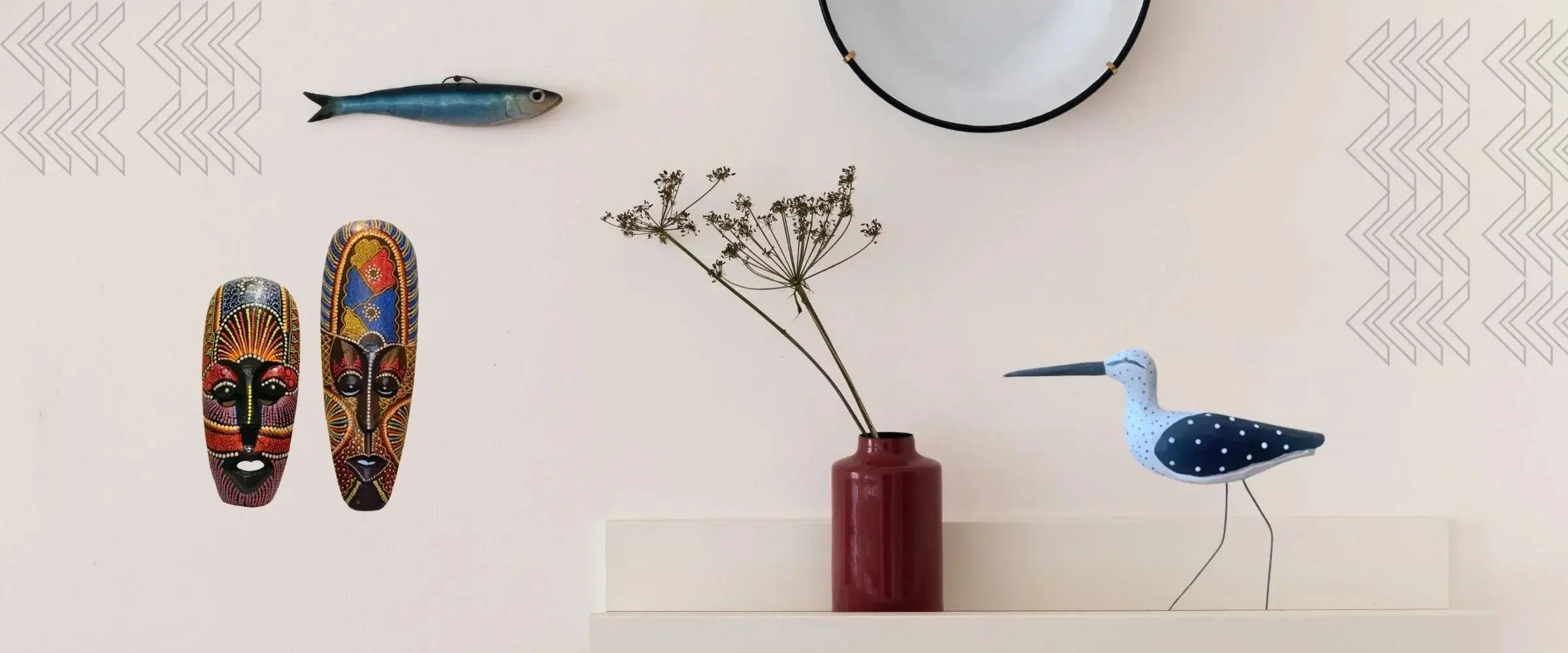 Handcrafted home decor with colorful tribal masks, wooden bird sculpture, dried flowers in red vase, and round wall mirror