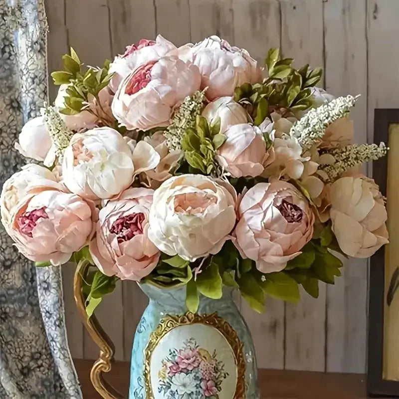 13 branches of realistic champagne peony silk flowers in a decorative vase with green foliage.