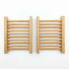 Two rectangular natural bamboo soap dishes with slatted drainage design on a white background.