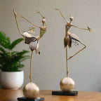 Two elegant gold-toned abstract dancing ballerina metal sculptures with layered patterned fabric skirts