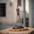 Bronze-colored abstract walking man sculpture with elongated limbs and textured metal surface on stone pedestal