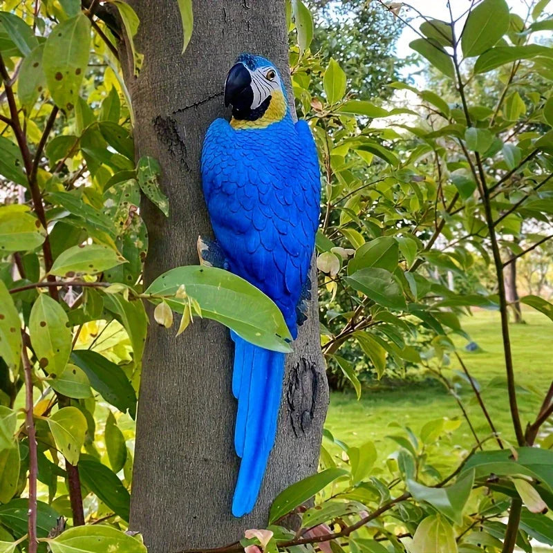 A vibrant blue and yellow handcrafted parrot statue perched realistically on a tree trunk in a garden setting.