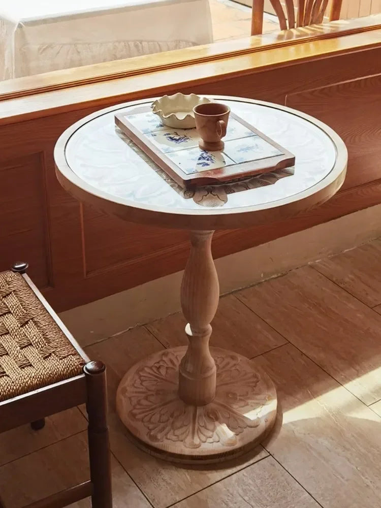 Small round wooden coffee table with a marble top and intricately carved pedestal base in natural wood finish