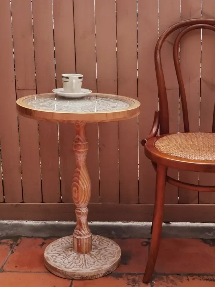 Small round wooden coffee table with a light carved top and intricately detailed pedestal base for elegant decor