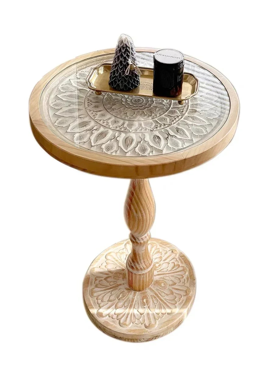 Small round wooden coffee table with carved floral base and clear glass top featuring intricate leaf design