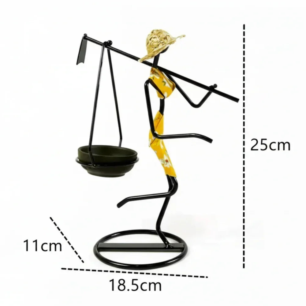 Black metal candle holder figurine of a woman in a yellow patterned dress and straw hat carrying a balance scale