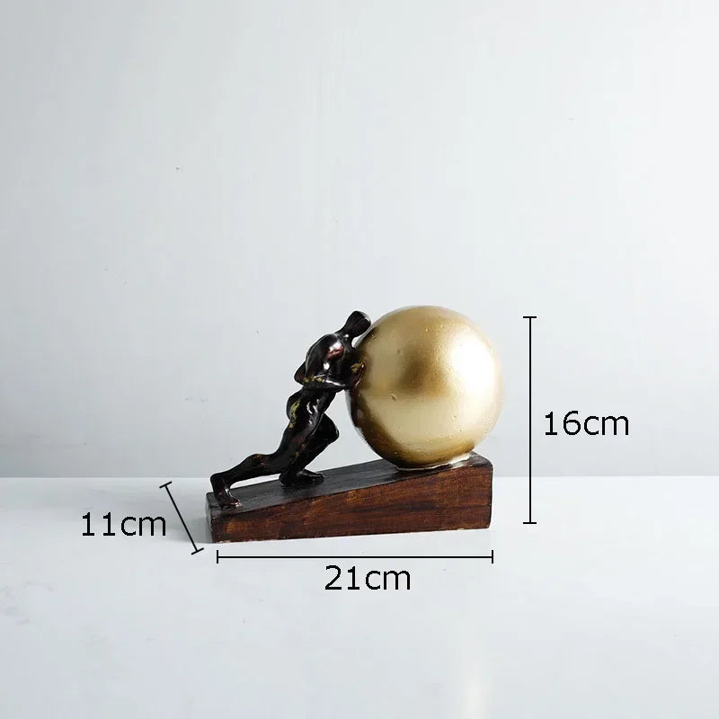 Bronze-colored metal figure statue of a man pushing a golden sphere on a dark wooden base for modern style home decor