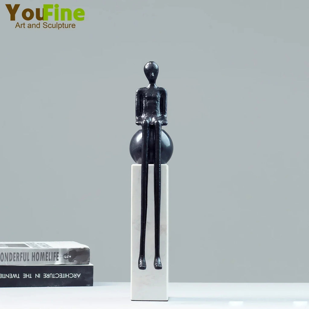 Black glossy luxury metal small figurine of seated humanoid with elongated limbs on white pedestal