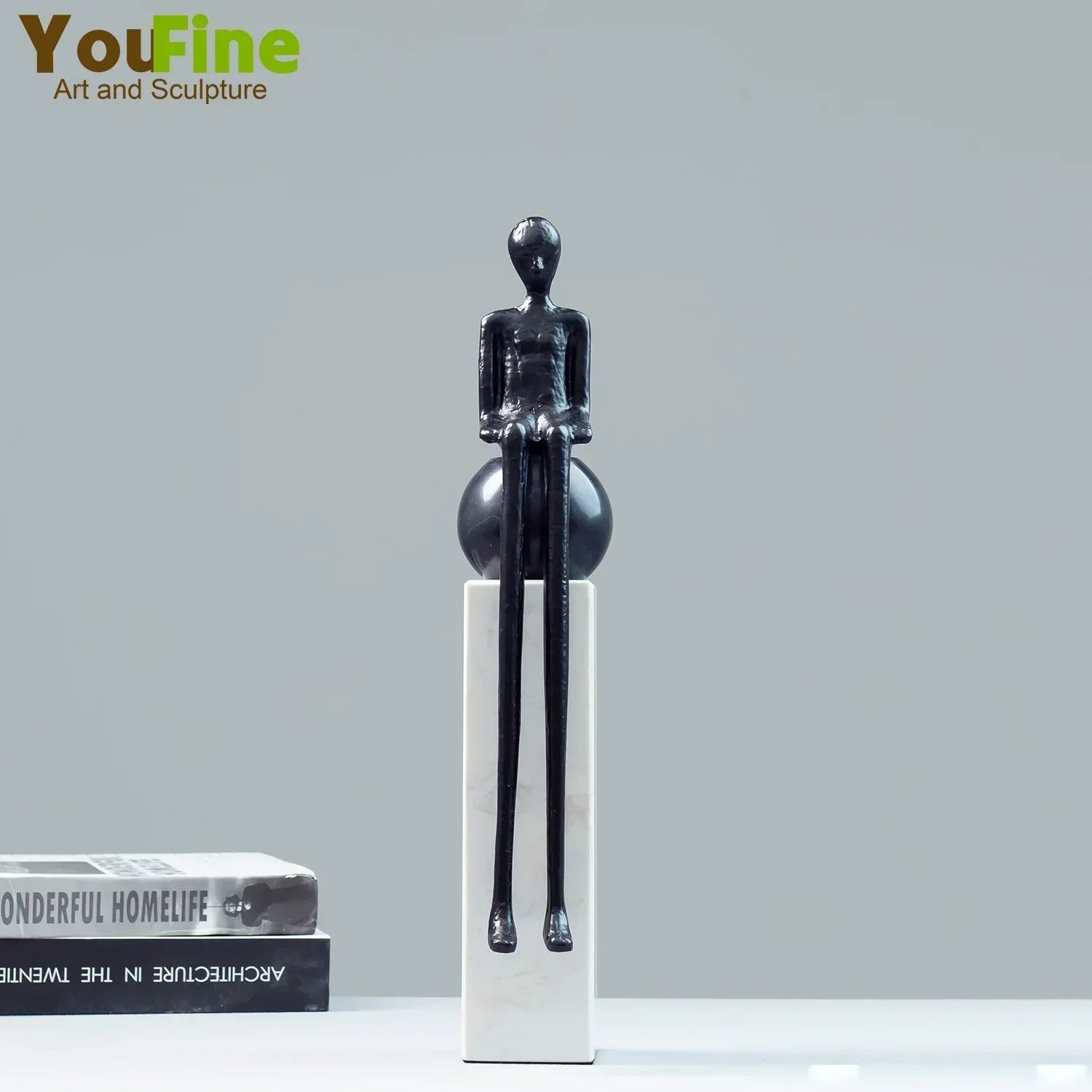 Black glossy luxury metal small figurine of seated humanoid with elongated limbs on white pedestal