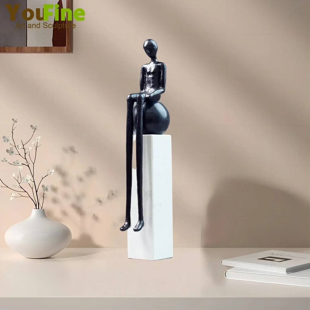Black glossy luxury metal small figurine of a seated humanoid with elongated limbs on a white pedestal
