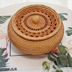 Woven rattan basket on a surface with a plant and magazine in the background