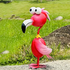 Handcrafted red metal flamingo garden sculpture with large eyes standing in a green garden. [[SKU:HOA-GSC-014]]