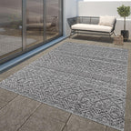 Anthracite outdoor rug with a textured high-low trellis pattern on a stone patio.