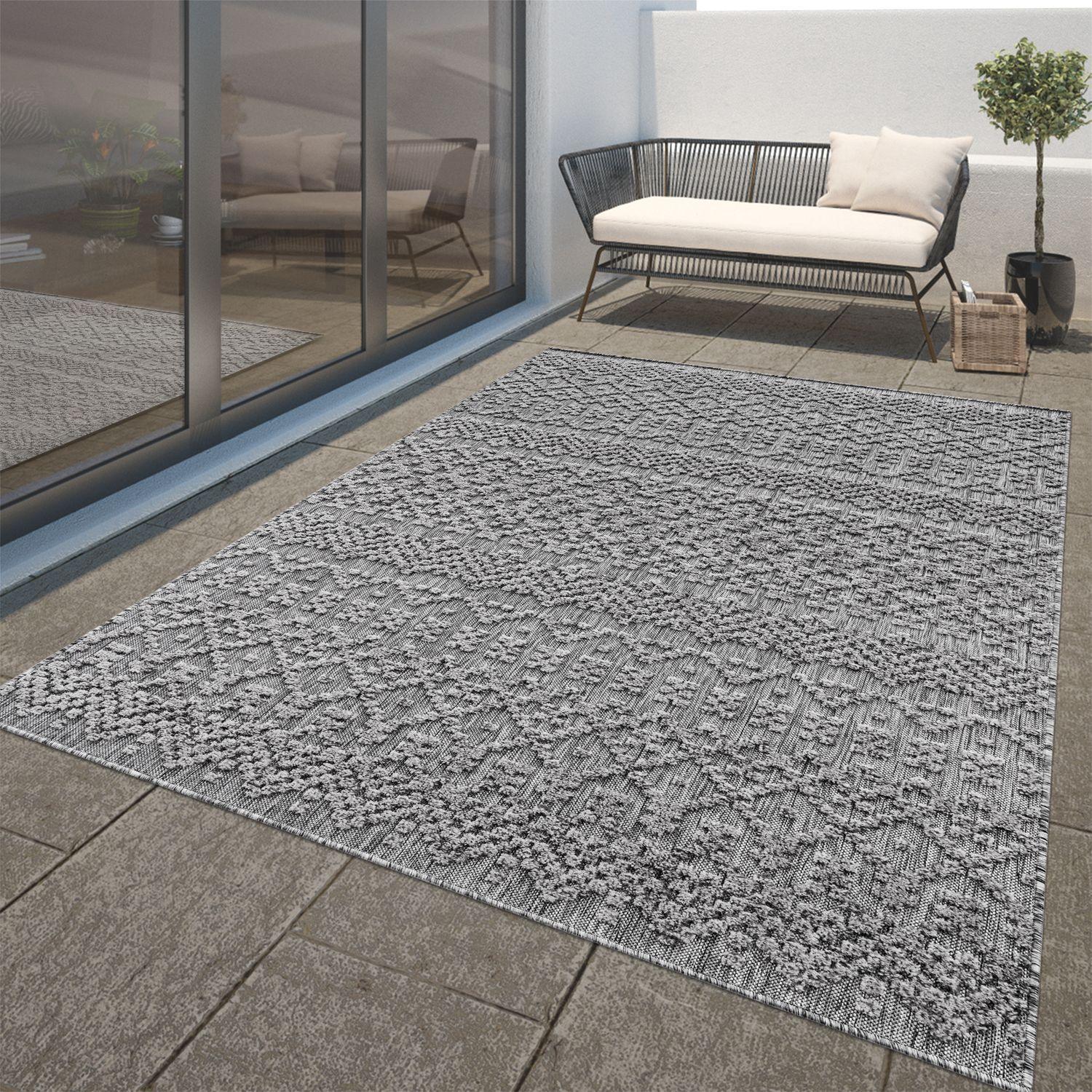 Anthracite outdoor rug with a textured high-low trellis pattern on a stone patio.