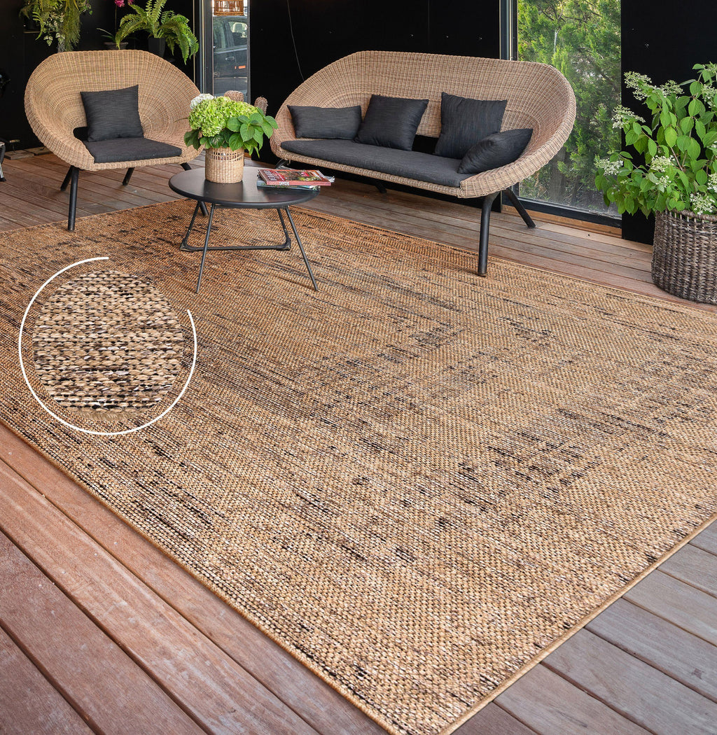 Rico braided look indoor and outdoor rug with a natural tan and black textured weave on a wooden patio deck.