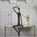 Large abstract sitting human sculpture metal figurine in black with elongated limbs in a contemplative pose on table