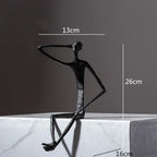 Large abstract sitting human sculpture in black textured metal with one arm raised in a modern sitting pose