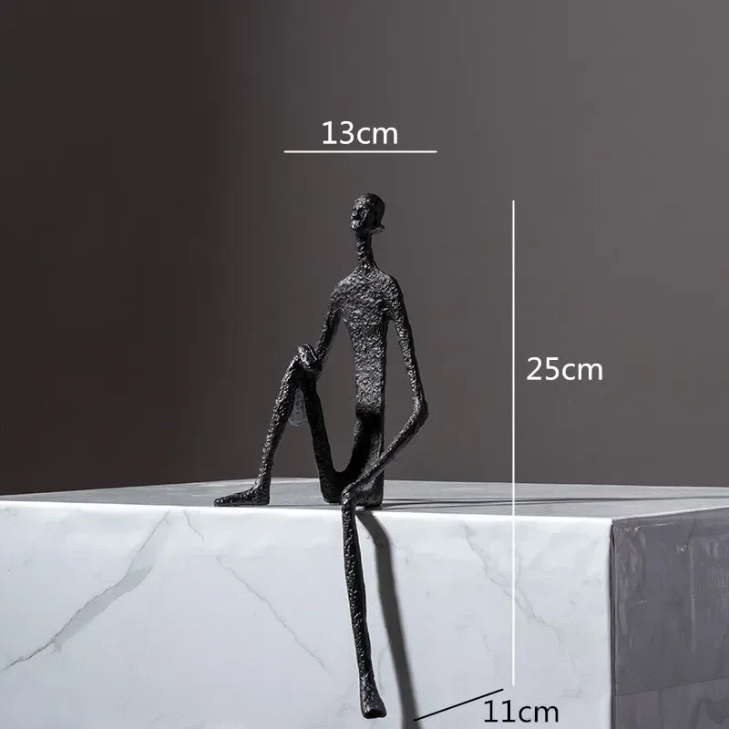 Large abstract sitting human sculpture black textured metal figurine seated on edge of white marble surface