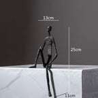Large abstract sitting human sculpture black textured metal figurine seated on edge of white marble surface