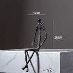 Large abstract sitting human sculpture in black textured metal with elongated limbs and minimalist design