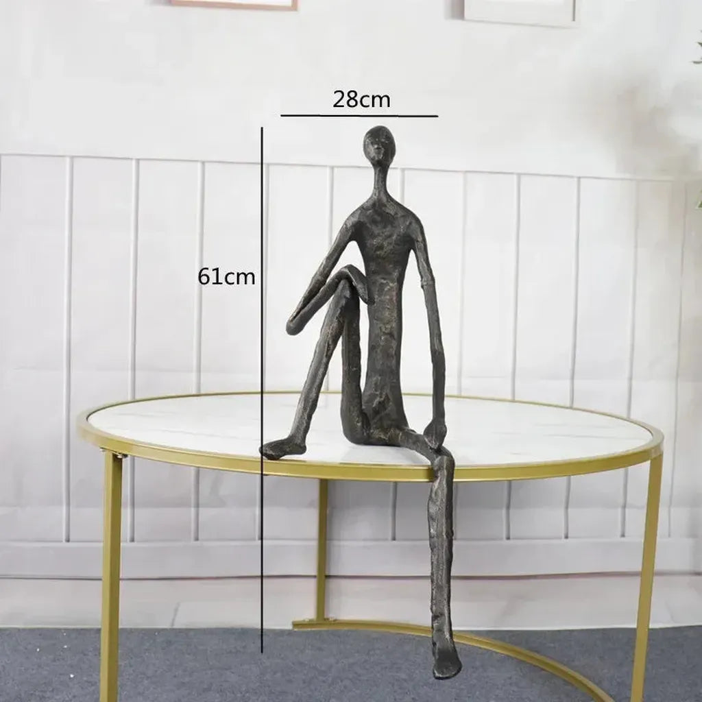 Large abstract sitting human sculpture in dark metal with elongated limbs on round table minimalist design