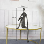 Large abstract sitting human sculpture in dark metal with elongated limbs on round table minimalist design