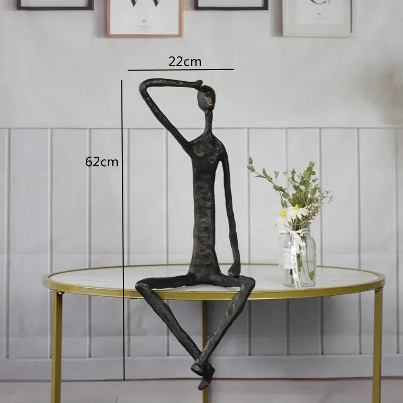 Large abstract sitting human sculpture in black metal with elongated limbs in a contemplative pose on a table