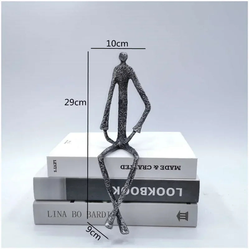 Large abstract sitting human sculpture with textured metallic finish atop stacked books in modern metal figurine design