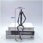 Large abstract sitting human sculpture with textured metallic finish atop stacked books in modern metal figurine design