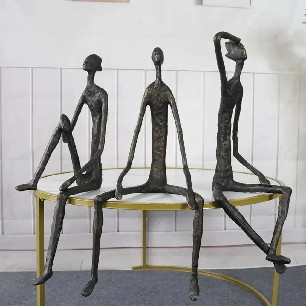 Large abstract sitting human sculpture featuring three bronze-colored metal figurines seated on a round table