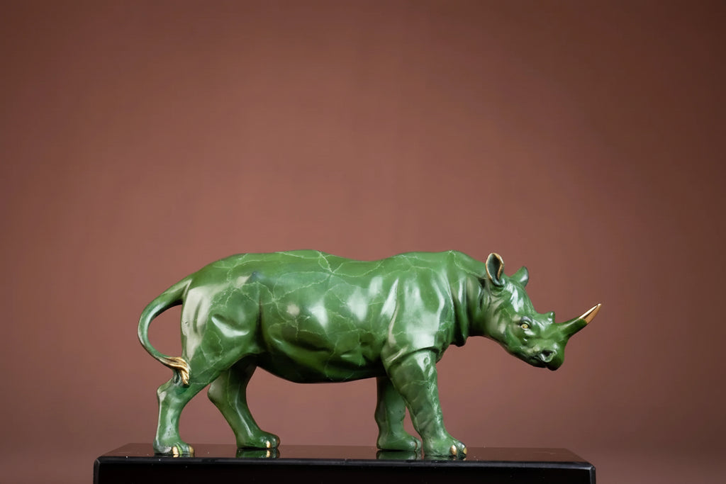 Luxury green rhinoceros statue with gold accents on horn and feet displayed on black pedestal for home and office decor