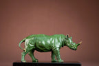 Luxury green rhinoceros statue with gold accents on horn and feet displayed on black pedestal for home and office decor