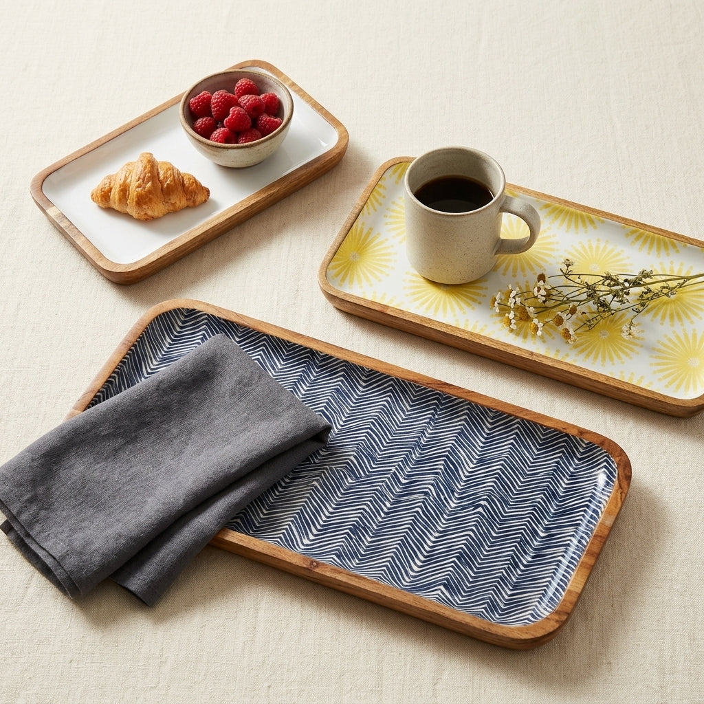 Three rectangular serving trays with light wood rims are arranged on a beige fabric surface. The trays have different printed patterns: one white with a yellow sunburst, one blue and white chevron, and one white with a yellow sunburst.