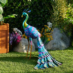 Colorful metal peacock statue with blue and green feathers standing on a lawn in a garden.