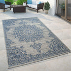 Blue and beige oriental floral medallion outdoor rug on a stone patio with outdoor furniture.