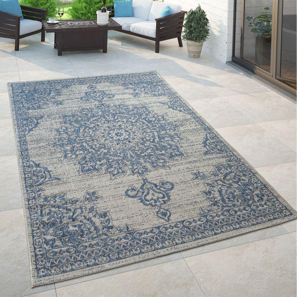 Blue and beige oriental floral medallion outdoor rug on a stone patio with outdoor furniture.