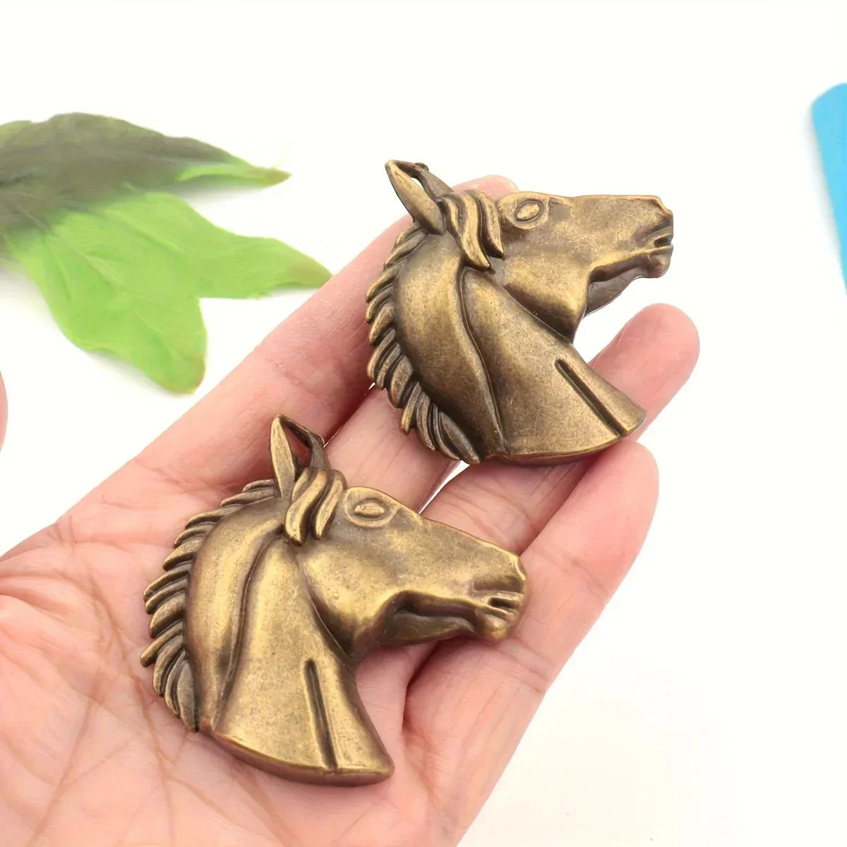 Two bronze horse head sculptures held in a hand with a white background