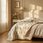 A beautifully styled bedroom featuring a quilted comforter with a tree pattern in muted green and beige, layered with a pink patterned throw blanket. The bed is dressed in cream-colored linens and set against a matching cream-colored wooden headboard.