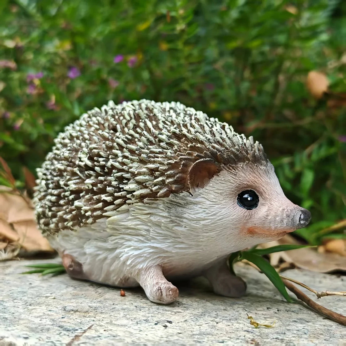 Realistic resin hedgehog figurine with detailed brown and white fur texture sitting on a stone in a garden. [[SKU:HOA-GSC-005]]