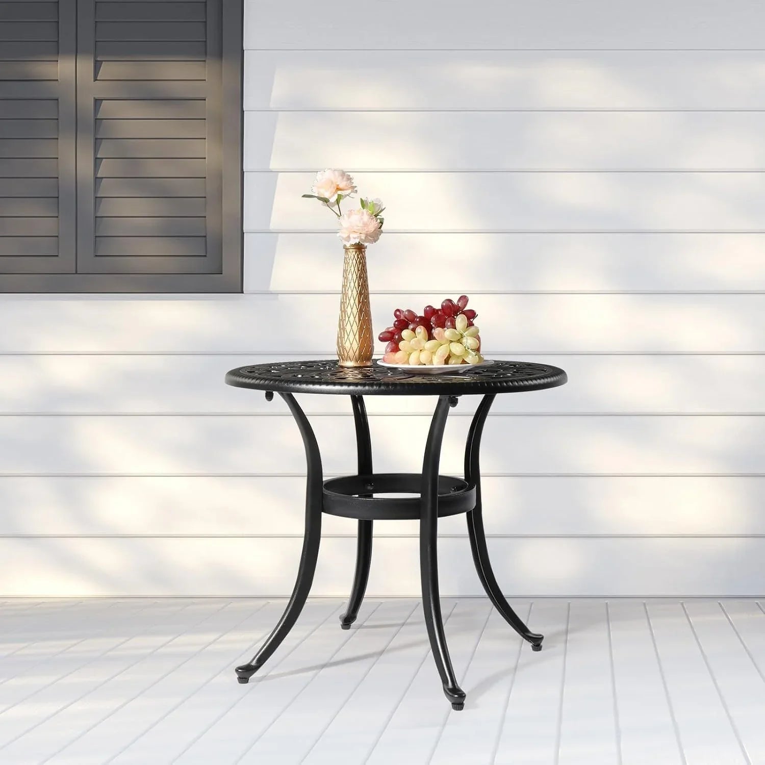 Black 23.6 inch round aluminum patio table with decorative lattice top and curved legs on a white porch.