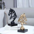 Two horse sculptures, one black and one gold, on a surface with books in the background.