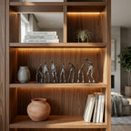 A tall wooden bookshelf with warm LED lighting in the compartments, styled with books, vases, and a row of metallic human figure sculptures on a middle shelf. [[SKU:HOA-SCU-012]]