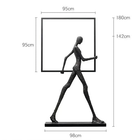 Black metal sculpture of a stylized human figure holding a square frame next to a comforting velvet sofa cushion for living room decor