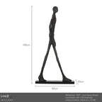 Black frp walker sculpture with elongated limbs and textured surface on iron base for living room home decor
