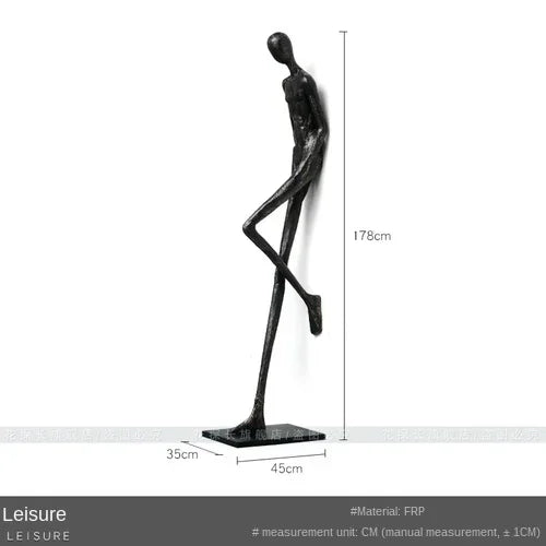 Black frp sculpture of a slender stylized human figure beside a large comforting velvet sofa cushion for living room decor