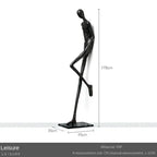 Black frp sculpture of a slender stylized human figure beside a large comforting velvet sofa cushion for living room decor