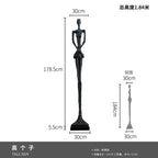 A tall slender black glass steel sculpture with elongated limbs paired with a comforting velvet sofa cushion for living room decor