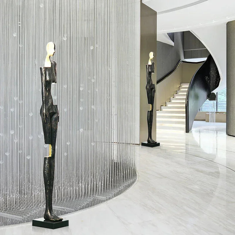 Black abstract sculpture with gold accents on black base displayed alongside large comforting velvet sofa cushion for living room decor